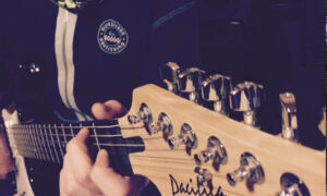 musik_13 Person spielt E-Gitarre mit Holzgriffbrett und silbernen Stimmwirbeln, naher Bildausschnitt.