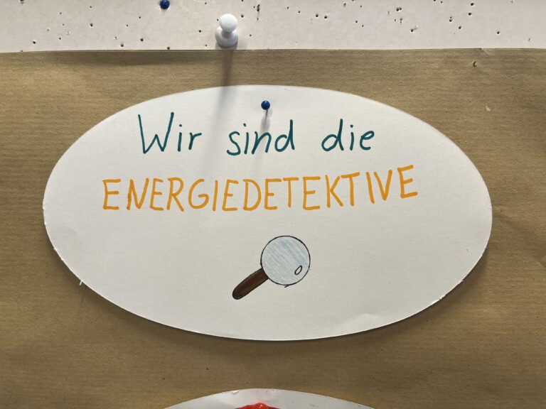 Schild mit Text Wir sind die Energiedetektive und einer gezeichneten Lupe.