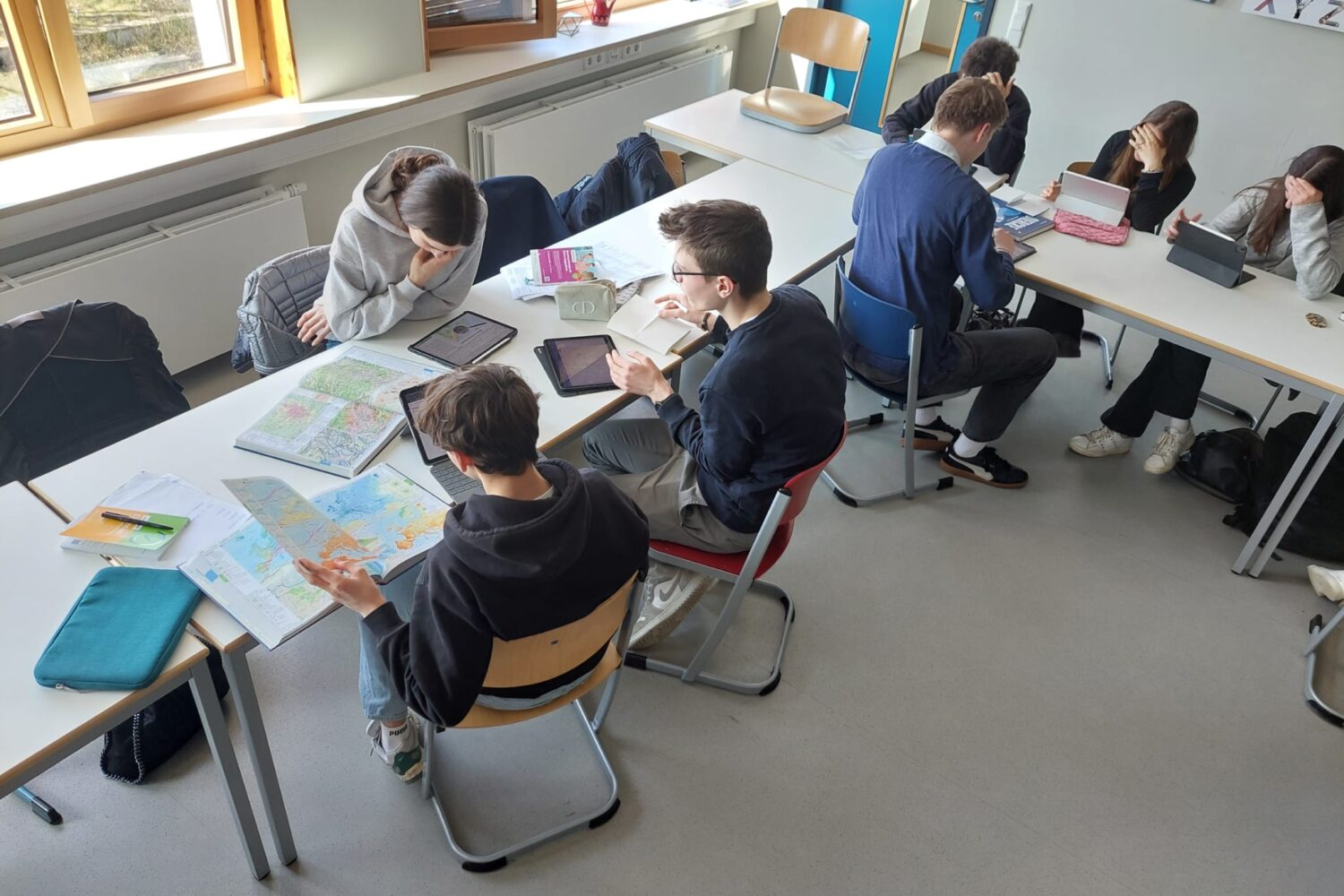 Schüler arbeiten in Gruppen an Tablets und Landkarten in einem Klassenraum.