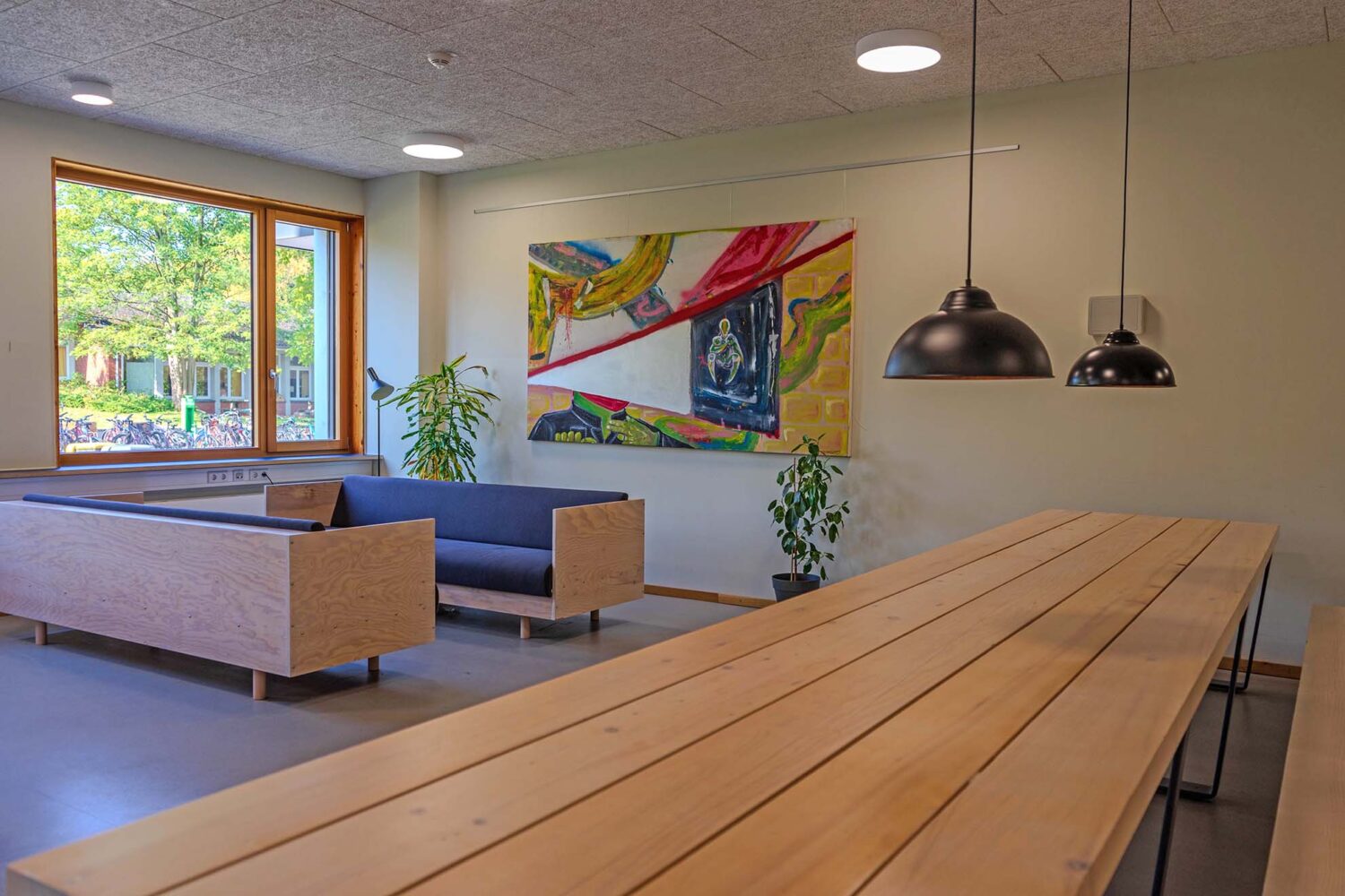Moderner Warteraum mit Kunst an der Wand, Holzbank, Fenster und Pflanzen.