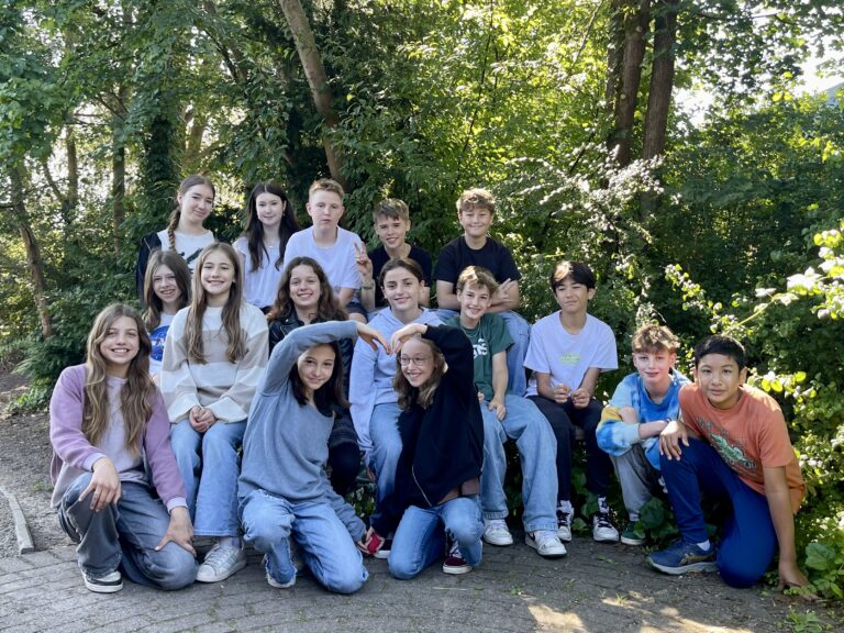 Gruppe von Jugendlichen posiert im Freien vor Bäumen, sie lächeln.