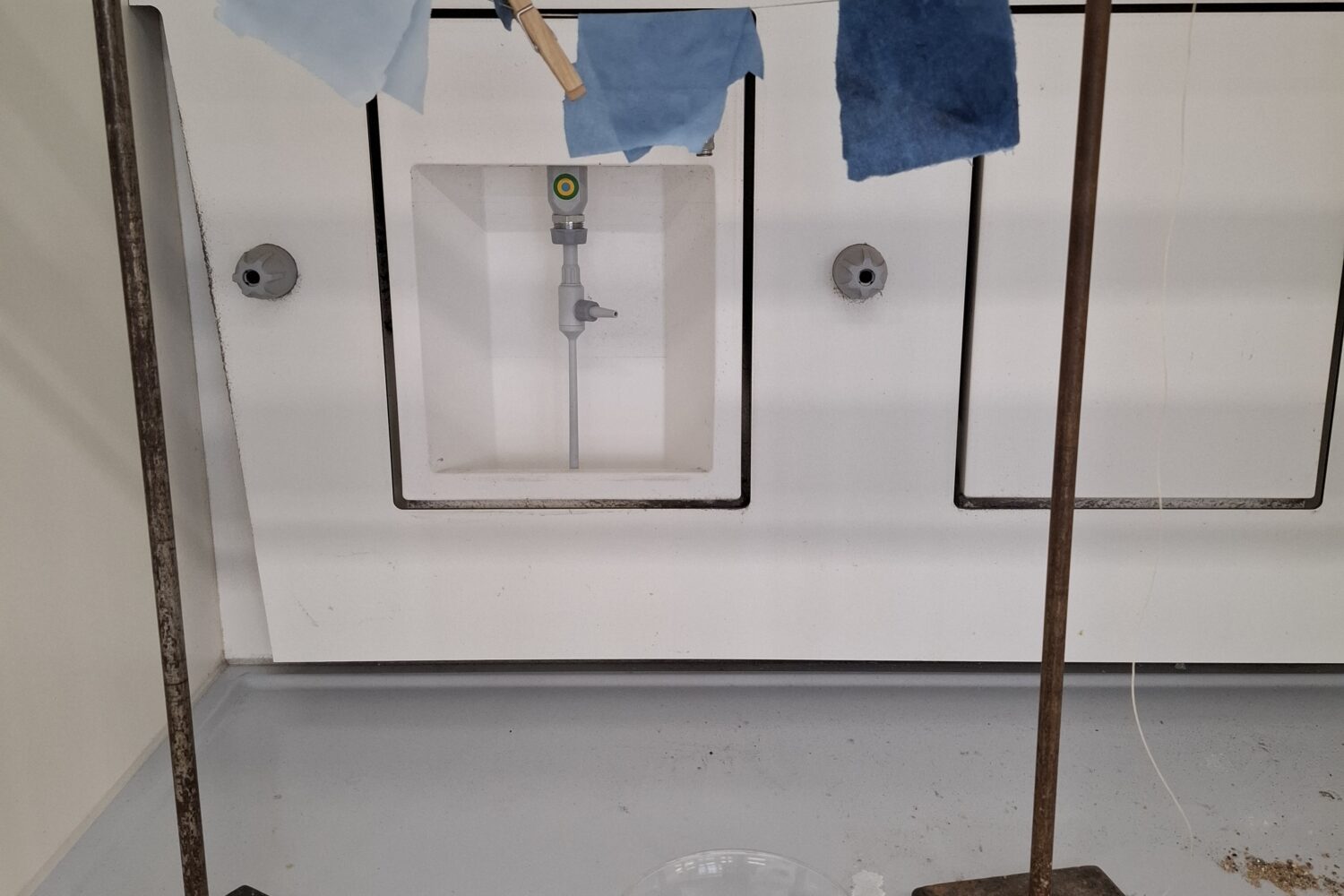 Blau gefärbte Stoffe aufgespannt, Bechergläser mit blauer Flüssigkeit darunter.