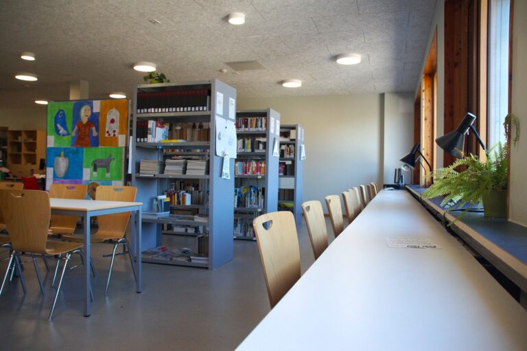 Ein heller Leseraum mit Bücherregalen, Tischen und Stühlen. Kunstwerke hängen an der Wand.