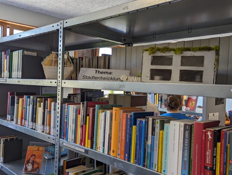 Bücherregal mit Schild Thema: Stadtentwicklung, Bücher und kleines Modellhaus auf dem Regal.