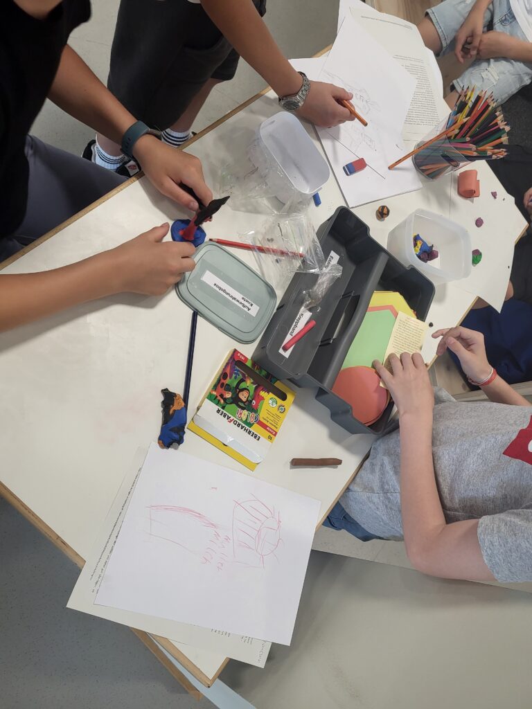 Kinder basteln zusammen an einem Tisch mit Papier, Buntstiften und Modelliermasse.