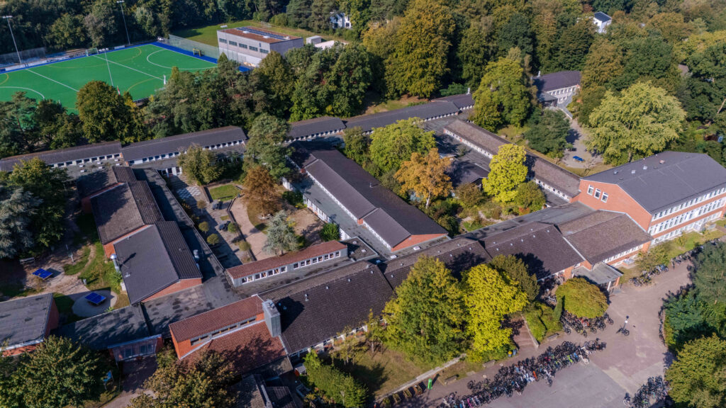 Luftbild einer weitläufigen Schulgebäudeanlage umgeben von Bäumen und Sportplätzen.