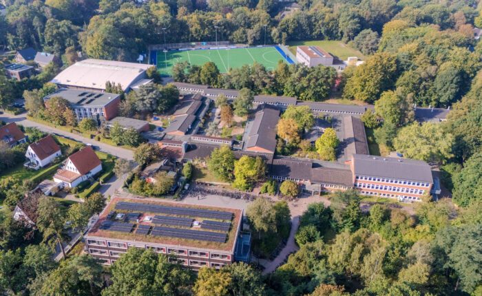 Luftaufnahme eines großen Schulgeländes mit Sportplatz und vielen Bäumen.