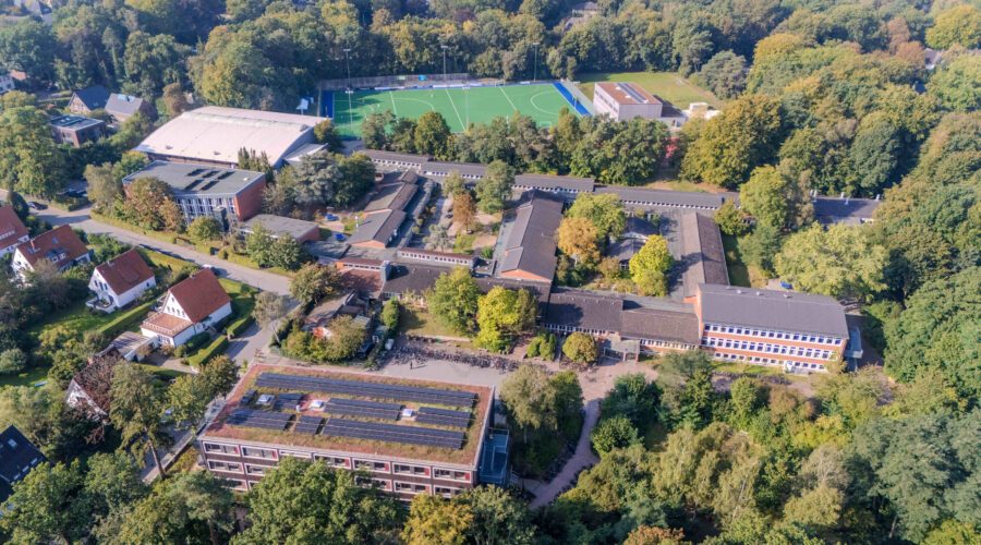 Luftaufnahme eines großen Schulgeländes mit Sportplatz und vielen Bäumen.