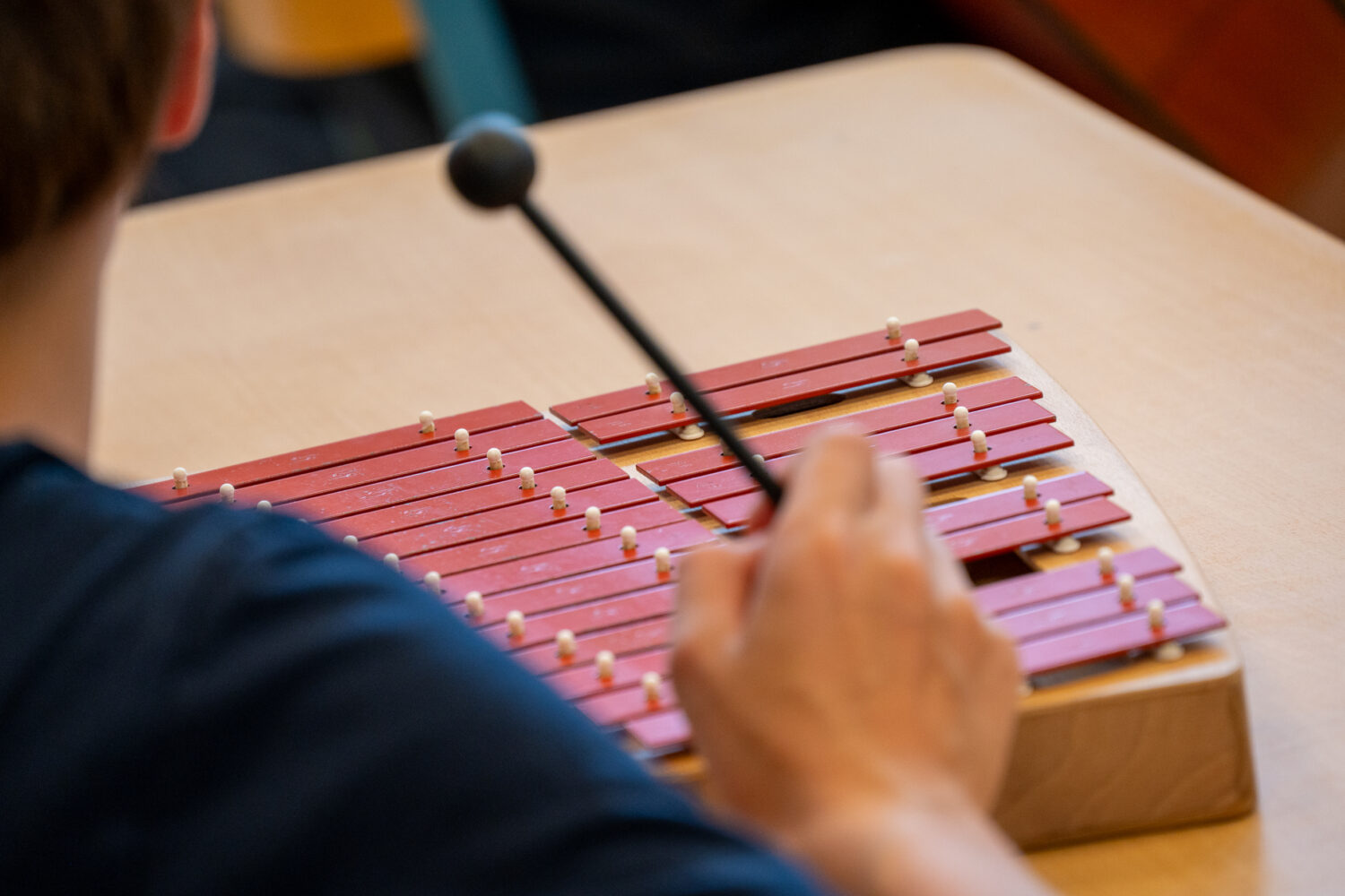 Person spielt Xylophon mit roten Klangplatten.