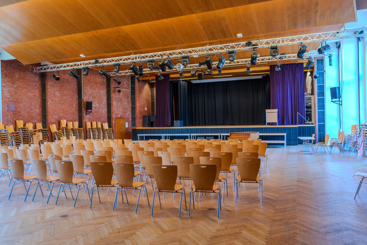 Ein leerer Veranstaltungssaal mit Bühne und aufgestellten Stuhlreihen.