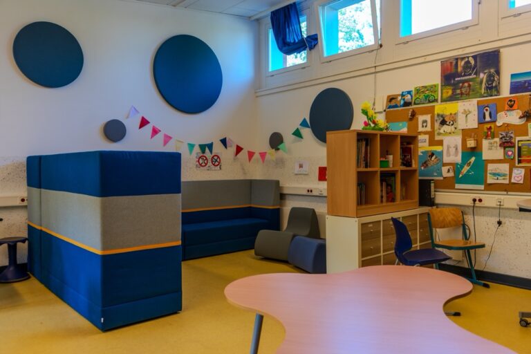 Moderner Klassenraum mit bunten Wänden, gemütlichen Sitzgelegenheiten und kreativer Wanddekoration.