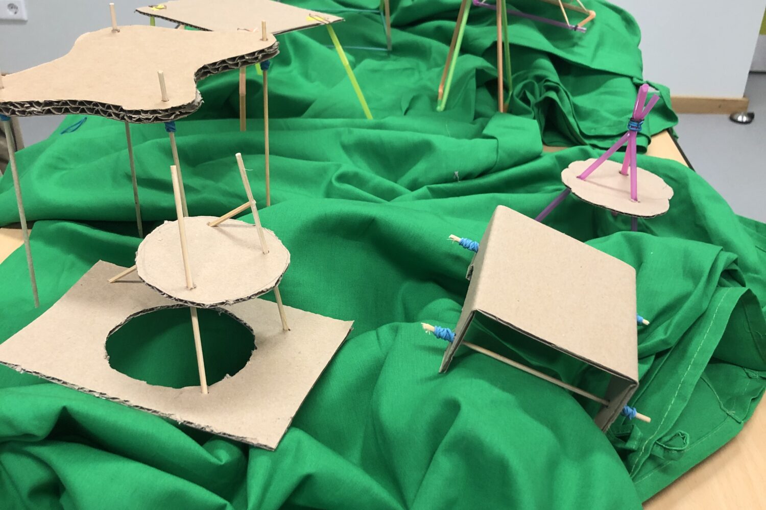 Pappstrukturen auf grüner Stoffunterlage, mit teils bunten Stützen aufgebaut.