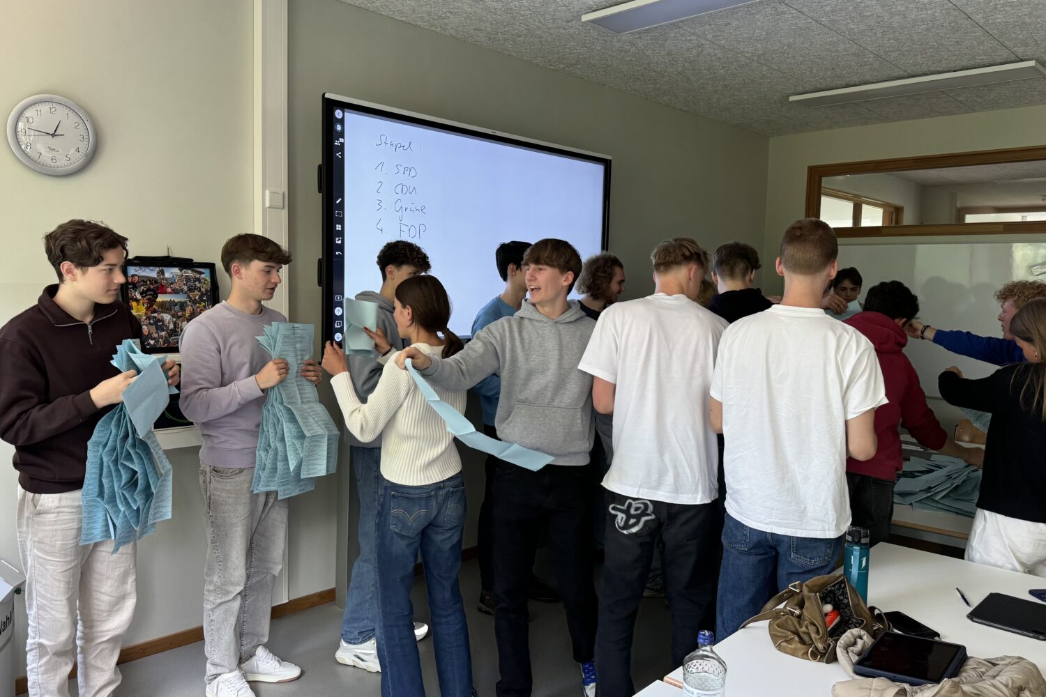 Gruppe junger Menschen sortiert blaue Stimmzettel in einem Klassenzimmer.