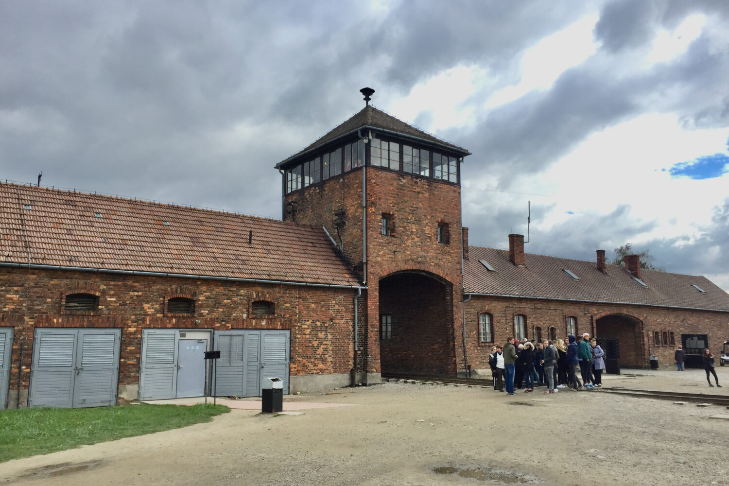 Gruppe von Menschen vor historischem Backsteingebäude bei bewölktem Himmel.