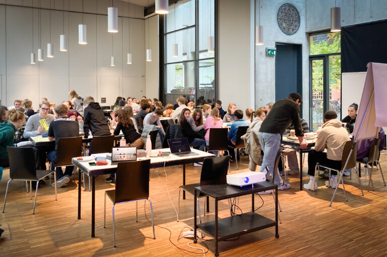 Große Gruppe junger Menschen in einem Konferenzraum mit Laptops und Flipchart.