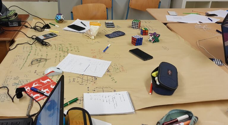 Ein Tisch mit Würfeln, Papieren, Stiften und elektronischen Geräten.