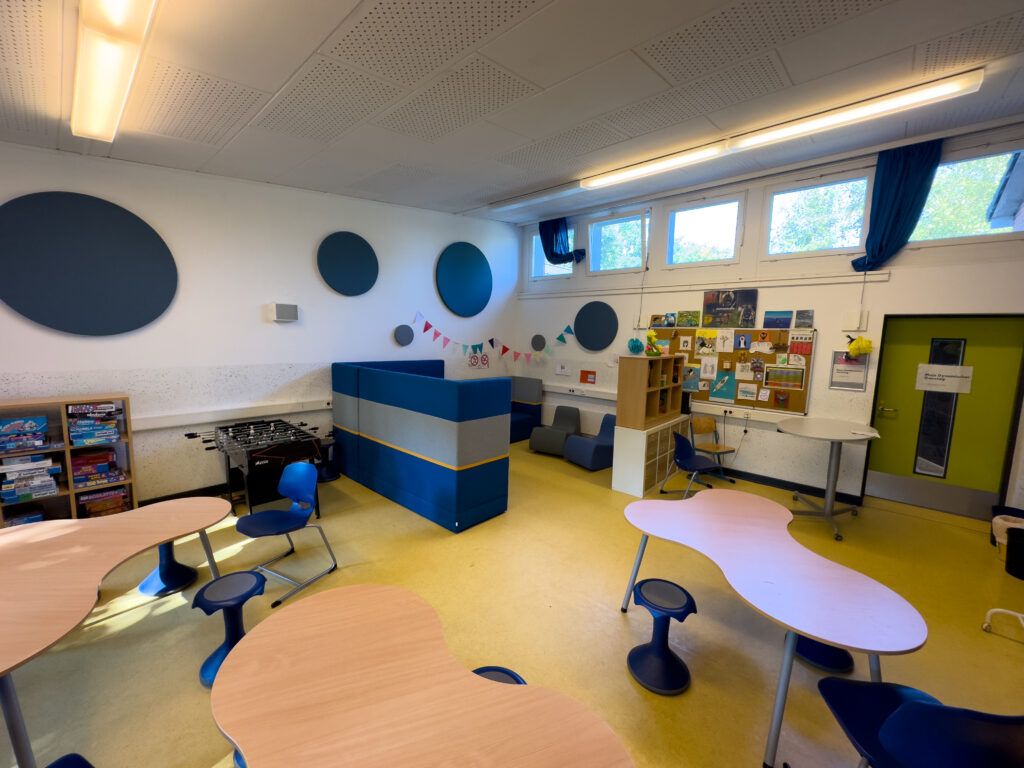 Moderner Klassenraum mit bunten Tischen, Pinnwand und Tischkicker.