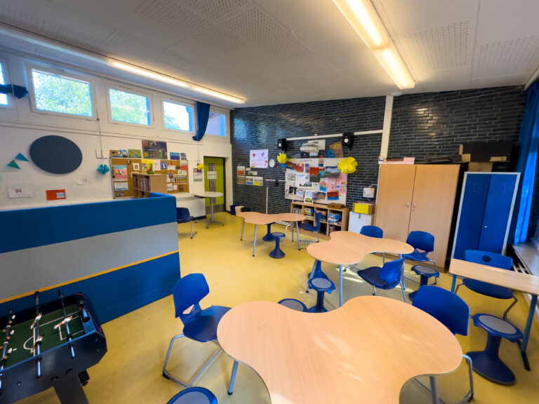 Klassenzimmer mit bunten Möbeln, Tischkicker und Pinnwänden an den Wänden.