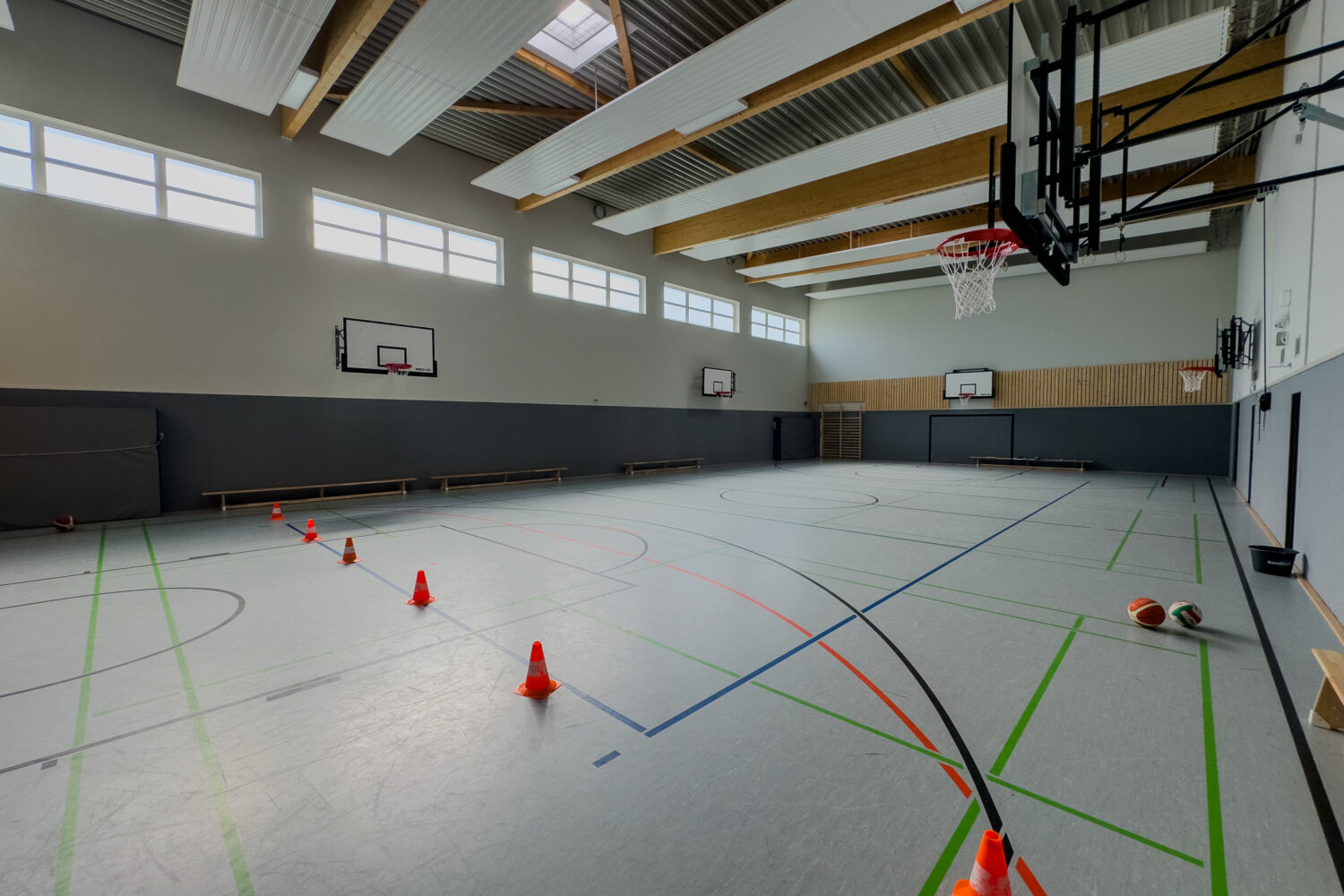 Leere Sporthalle mit Basketballkörben, Verkehrshütchen und Bällen auf dem Boden.
