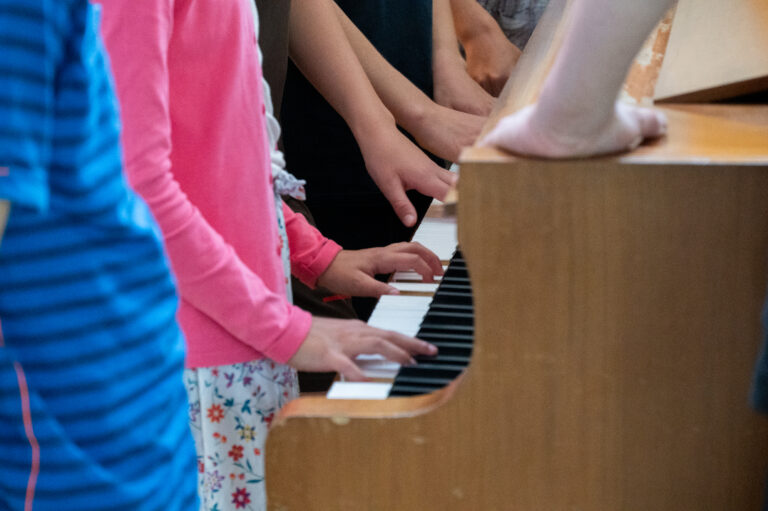 Kinderhände spielen zusammen auf einem Klavier.