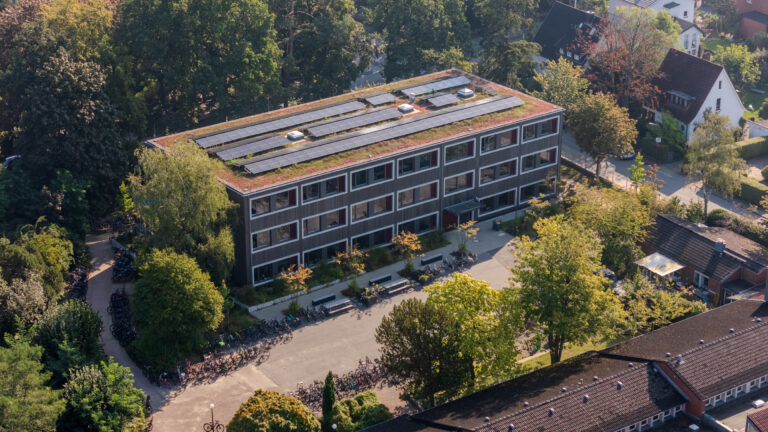 Modernes Gebäude mit begrüntem Dach und Solaranlagen, umgeben von Bäumen und Fahrrädern.