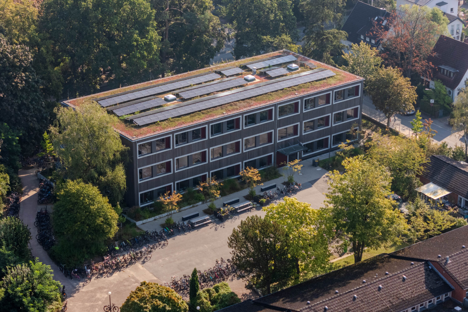 Luftaufnahme eines Gebäudes mit begrüntem Dach und Solarmodulen, umgeben von Bäumen.