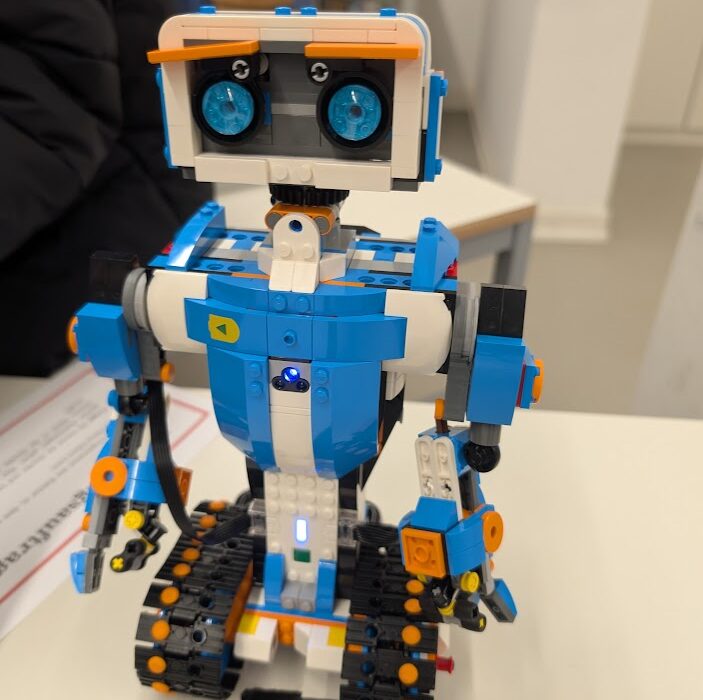 Bunter Roboter aus Bauklötzen auf einem Tisch mit Schienenbändern und leuchtenden Augen.