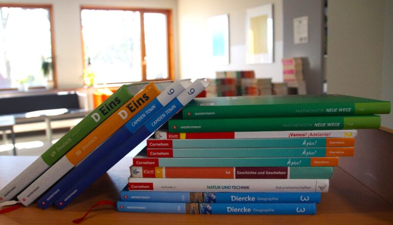 Ein Stapel Schulbücher auf einem Tisch in einem hellen Raum.