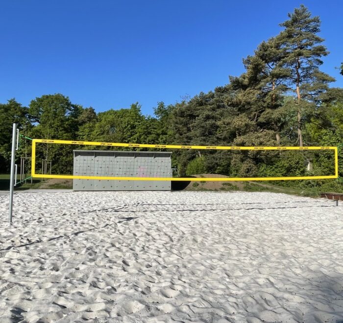 Sandvolleyballfeld mit gelbem Netz und einer Wand im Hintergrund.