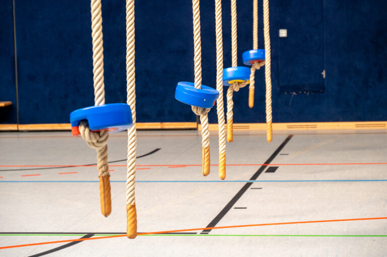 Kletterseile mit blauen Scheiben in einer Turnhalle vor dunkelblauer Wand.
