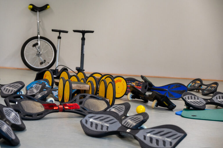 Verschiedene Sportgeräte auf dem Boden: Einrad, Roller und Balanceboard.