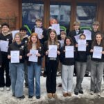 Gruppe von Jugendlichen hält Urkunden, lächelt vor einem Gebäude im Schnee.