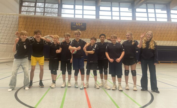 Ein Volleyballteam mit zehn Jugendlichen, die lächelnd in der Sporthalle posieren.