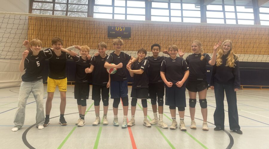 Ein Volleyballteam mit zehn Jugendlichen, die lächelnd in der Sporthalle posieren.