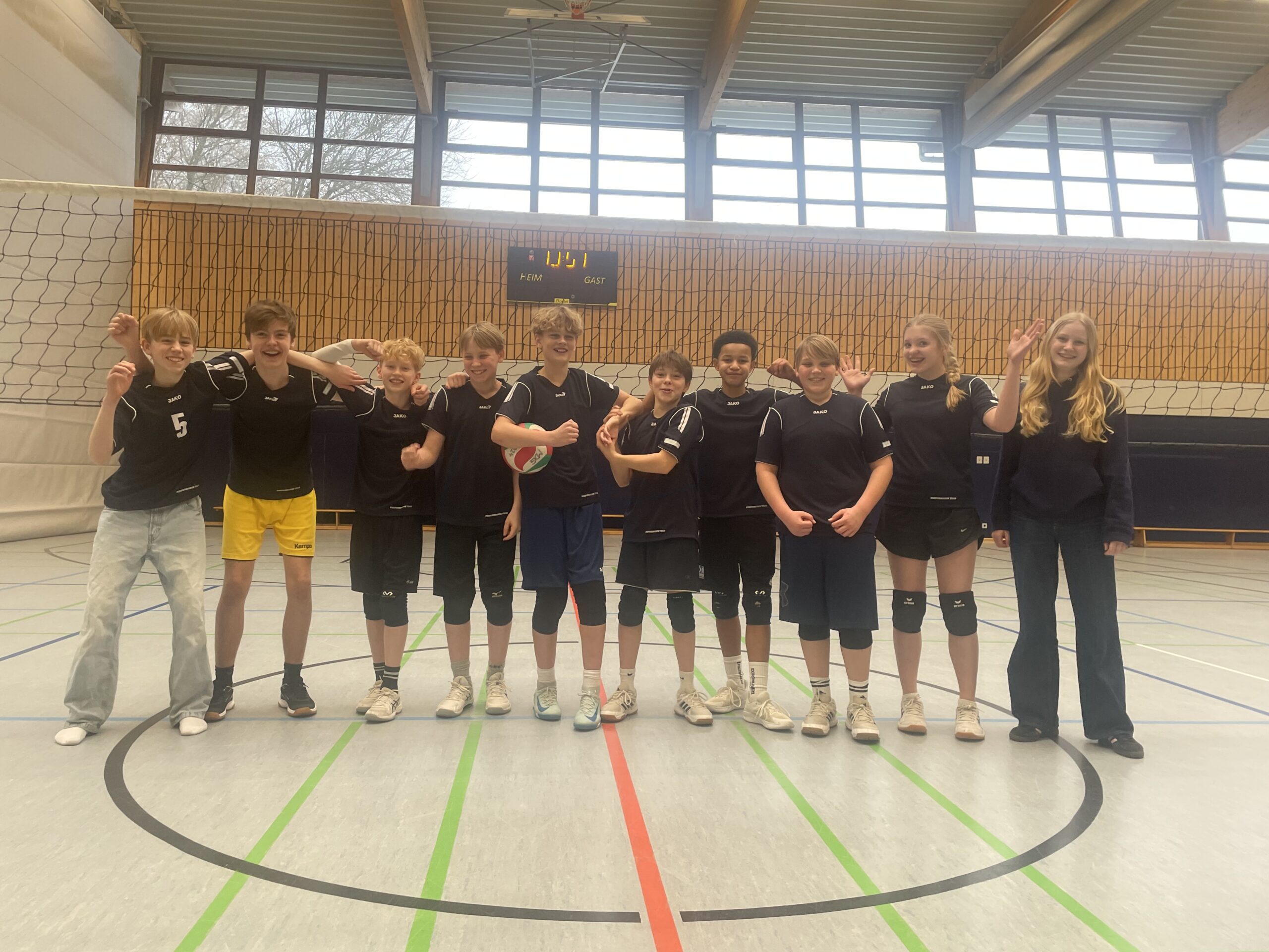 Ein Volleyballteam mit zehn Jugendlichen, die lächelnd in der Sporthalle posieren.