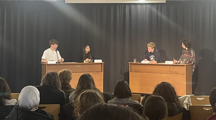 Diskussionstisch mit mehreren jungen Menschen, die auf ein Publikum blicken.