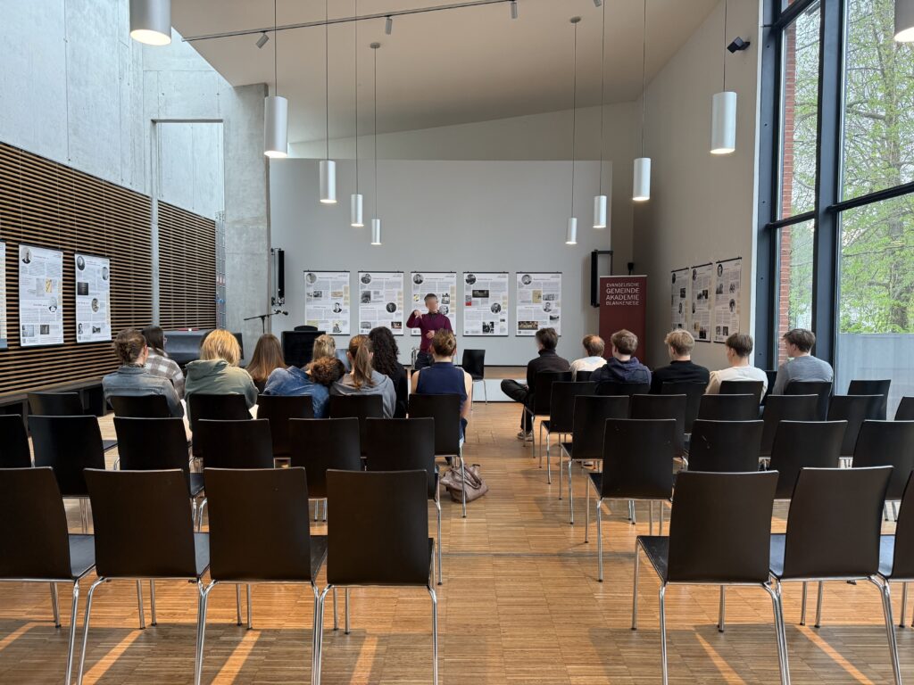 Ein Mann steht vor einer Gruppe von Personen in einem hellen, modernen Raum.