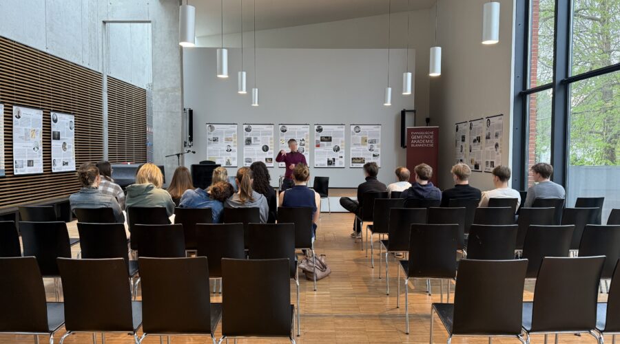 Ein Mann steht vor einer Gruppe von Personen in einem hellen, modernen Raum.