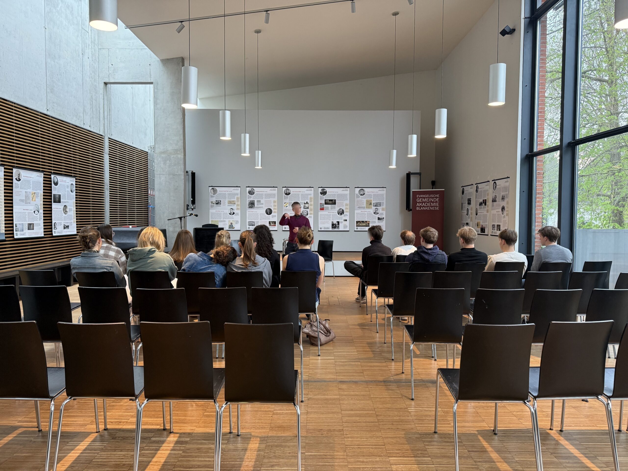 Ein Mann steht vor einer Gruppe von Personen in einem hellen, modernen Raum.