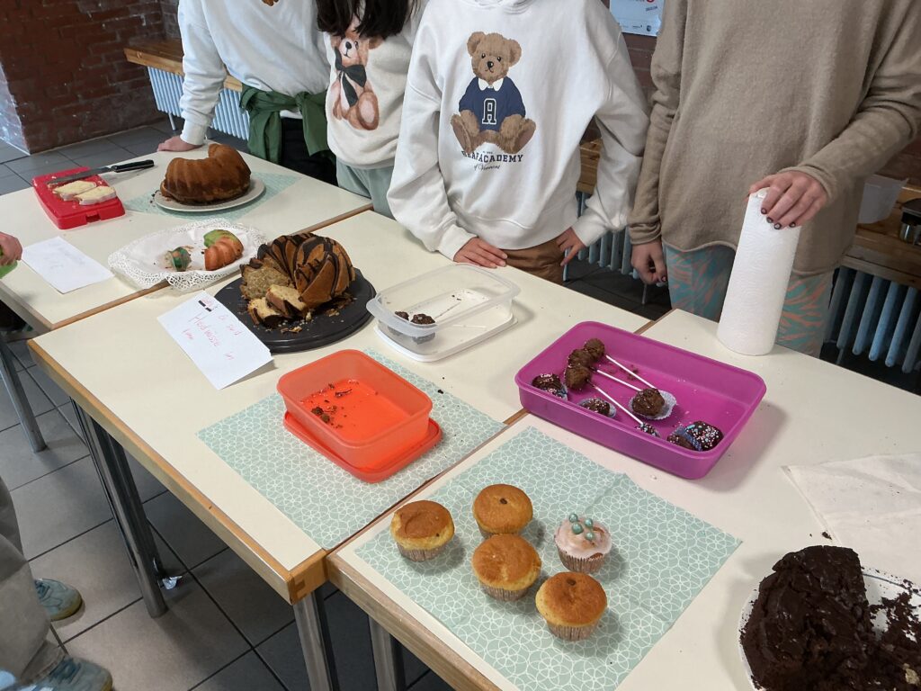 Eine Person mit einem Bärenmotiv auf dem Pullover steht an einem Tisch mit Kuchen.