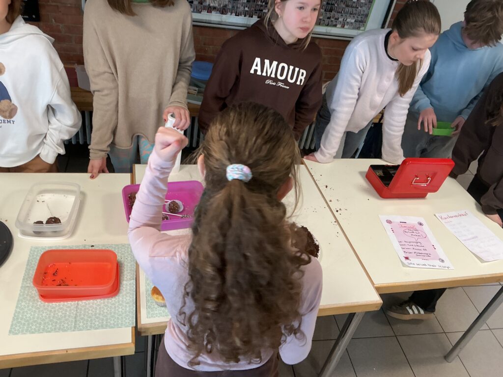 Eine Person mit langen, lockigen Haaren hebt eine Hand über einen Tisch mit Snacks.