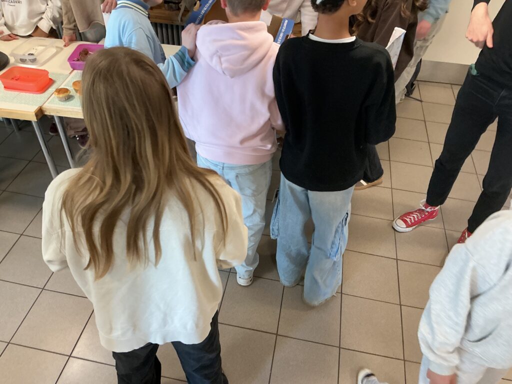 Eine Person mit langen, braunen Haaren trägt ein weißes Sweatshirt und schwarze Hosen.