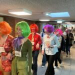 Eine Gruppe von Personen in bunten Perücken und Kostümen, die einen Flur entlangläuft.