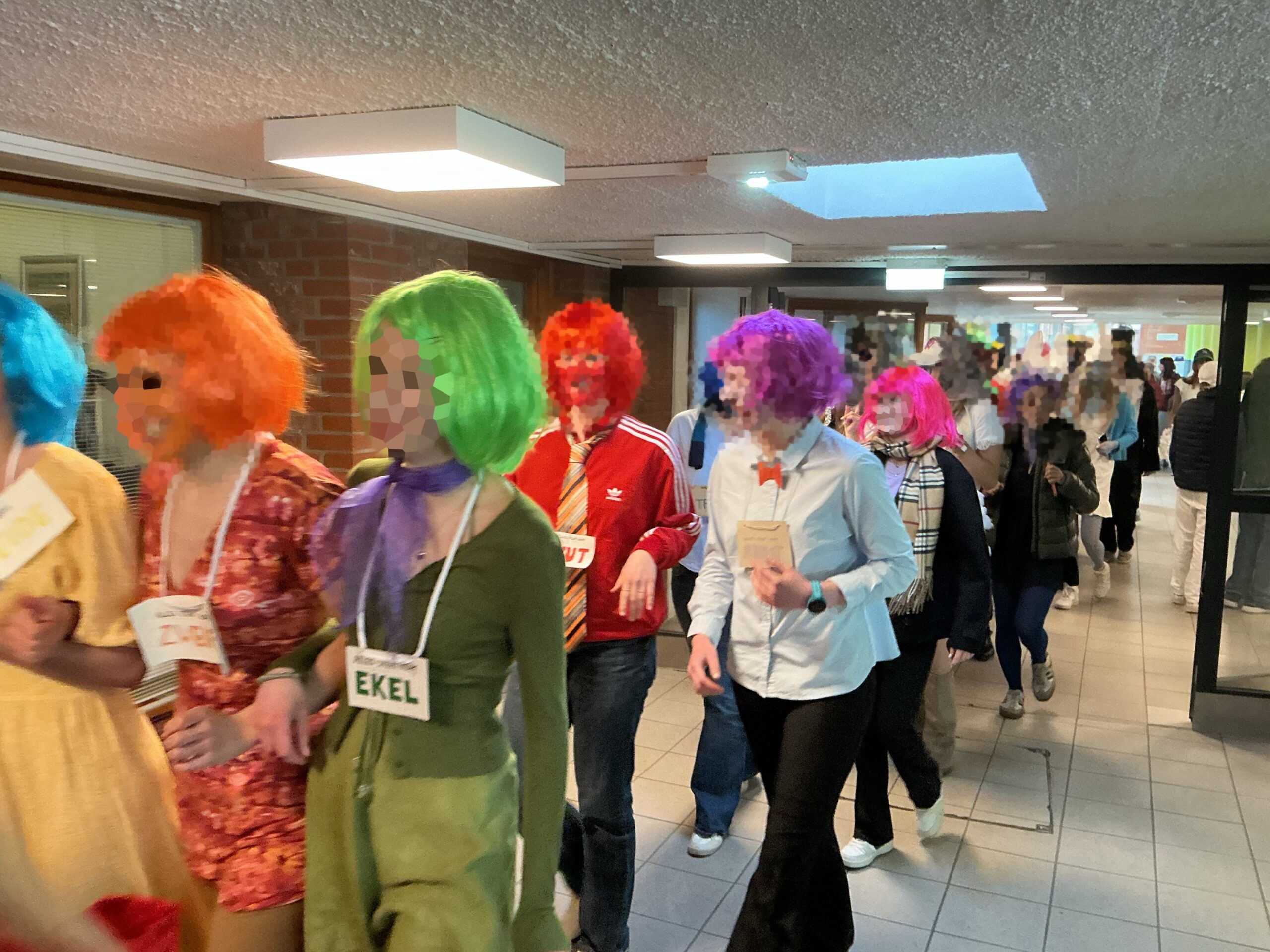 Eine Gruppe von Personen in bunten Perücken und Kostümen, die einen Flur entlangläuft.