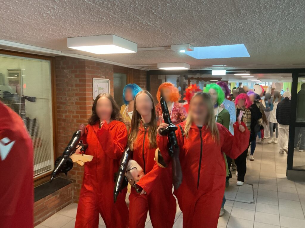 Drei Personen in roten Overalls halten Spielzeugwaffen und gehen in einem Flur.