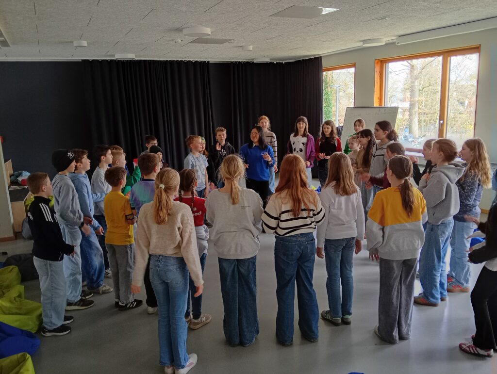 Eine Gruppe von Kindern steht im Kreis in einem Raum und interagiert miteinander.