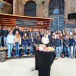 Eine Gruppe von Jugendlichen posiert lächelnd vor einer vorderen Bühne in einem Veranstaltungsort.