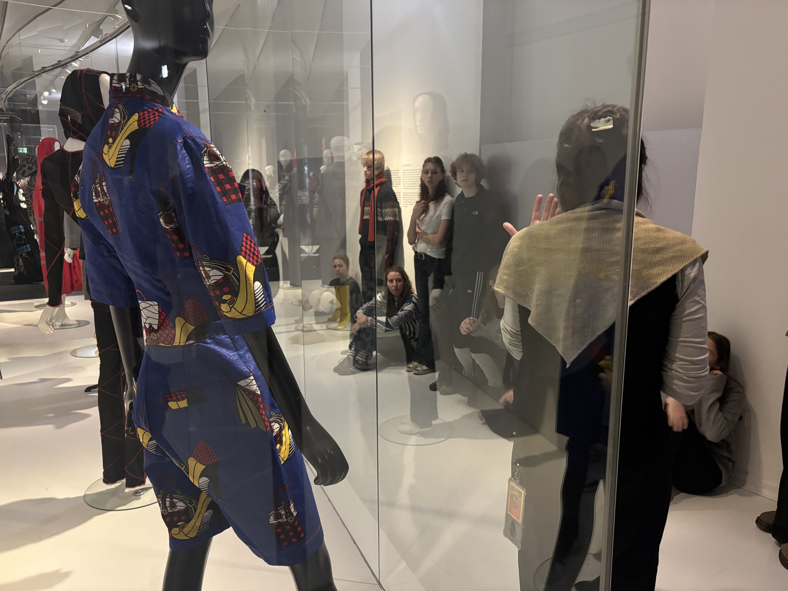 Dunkelhäutige Person mit blauem, gemustertem Outfit steht vor einer Glasscheibe.