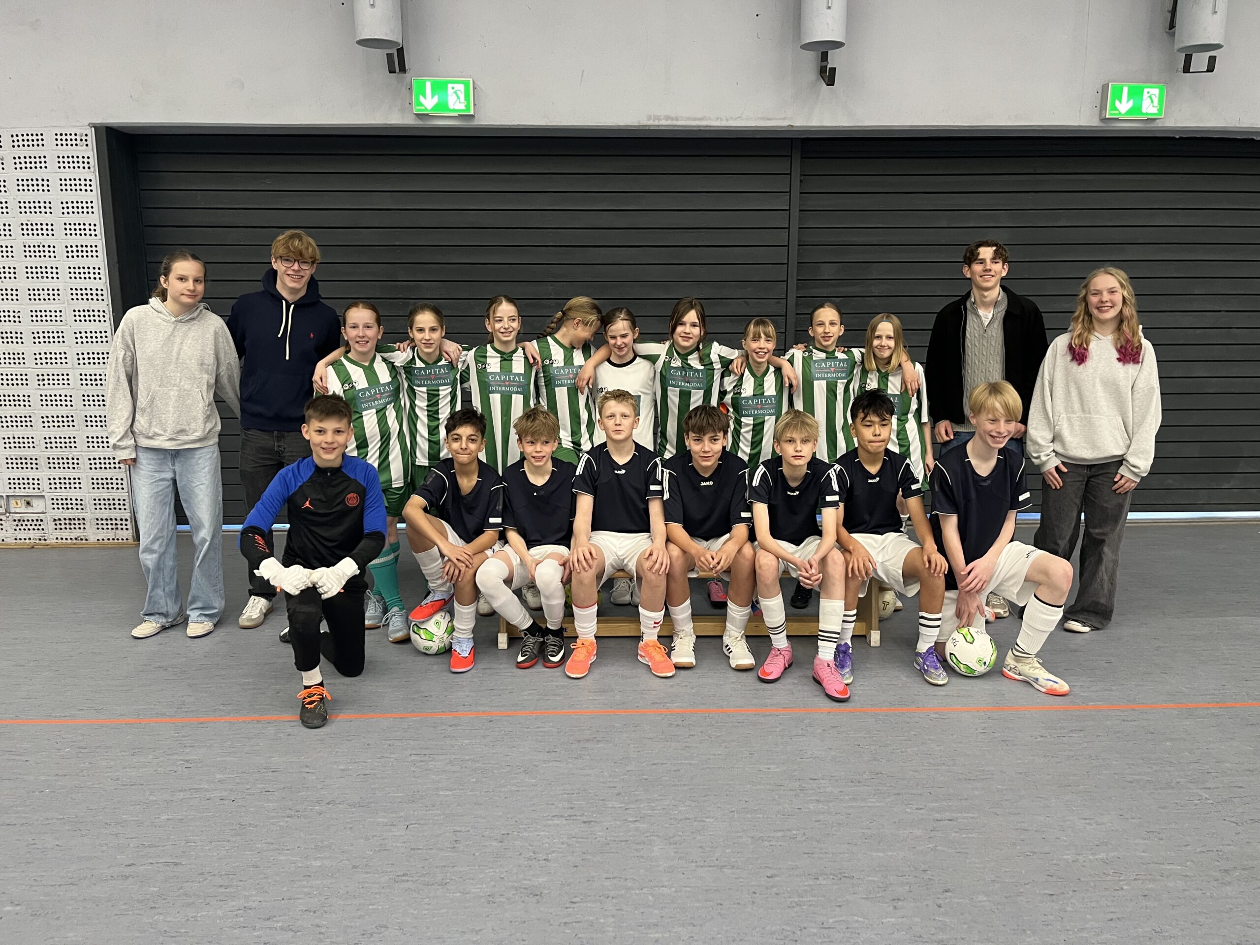 Gruppenscreenshot mit Jungen und Mädchen in Sportkleidung, die fröhlich in einer Halle posieren.