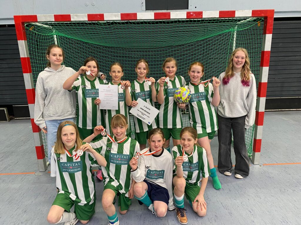 Mädchenmannschaft feiert mit Medaillen und Pokalen in einer Sporthalle.